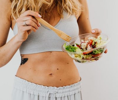 Young woman in sports attire holding a fresh salad bowl, promoting a healthy lifestyle.