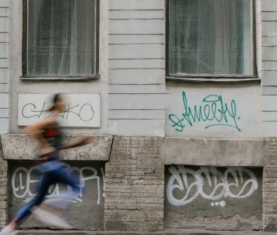 Blurred motion of a woman running past a graffiti-covered urban wall. Captures dynamic energy.