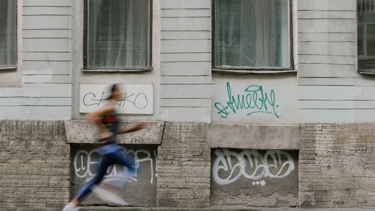 Blurred motion of a woman running past a graffiti-covered urban wall. Captures dynamic energy.